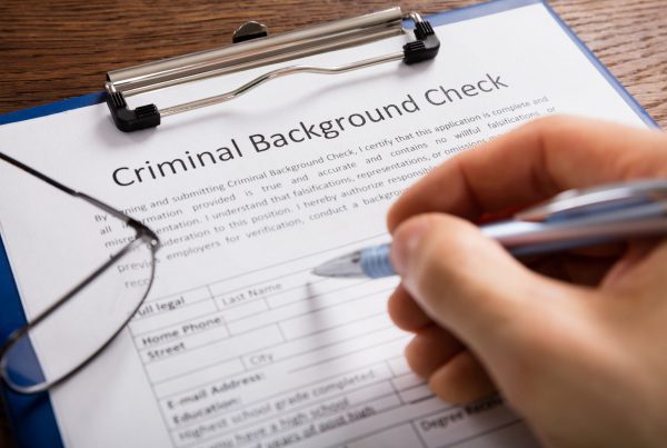 Close-up Of Person Hand Filling Criminal Background Check Application Form