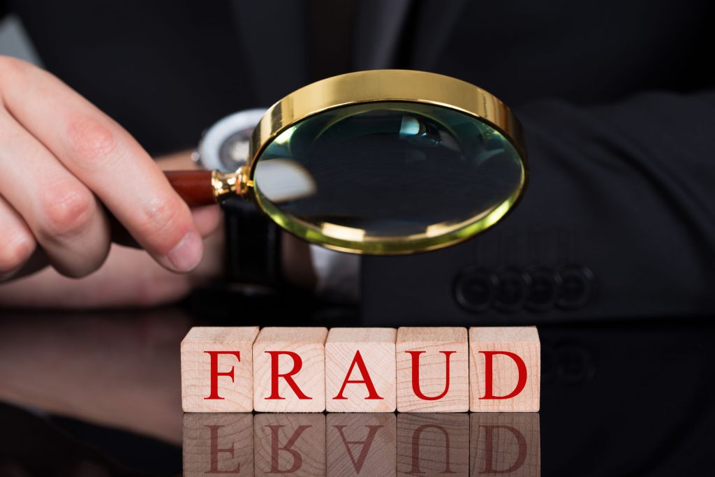 Cropped image of young businessman examining Fraud blocks through magnifying glass on desk