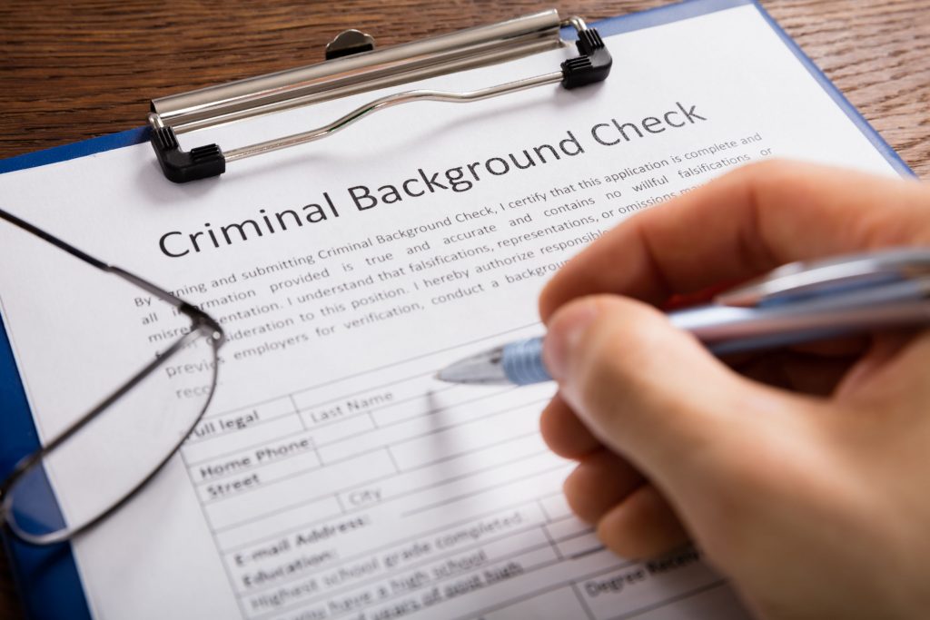 Close-up Of Person Hand Filling Criminal Background Check Application Form